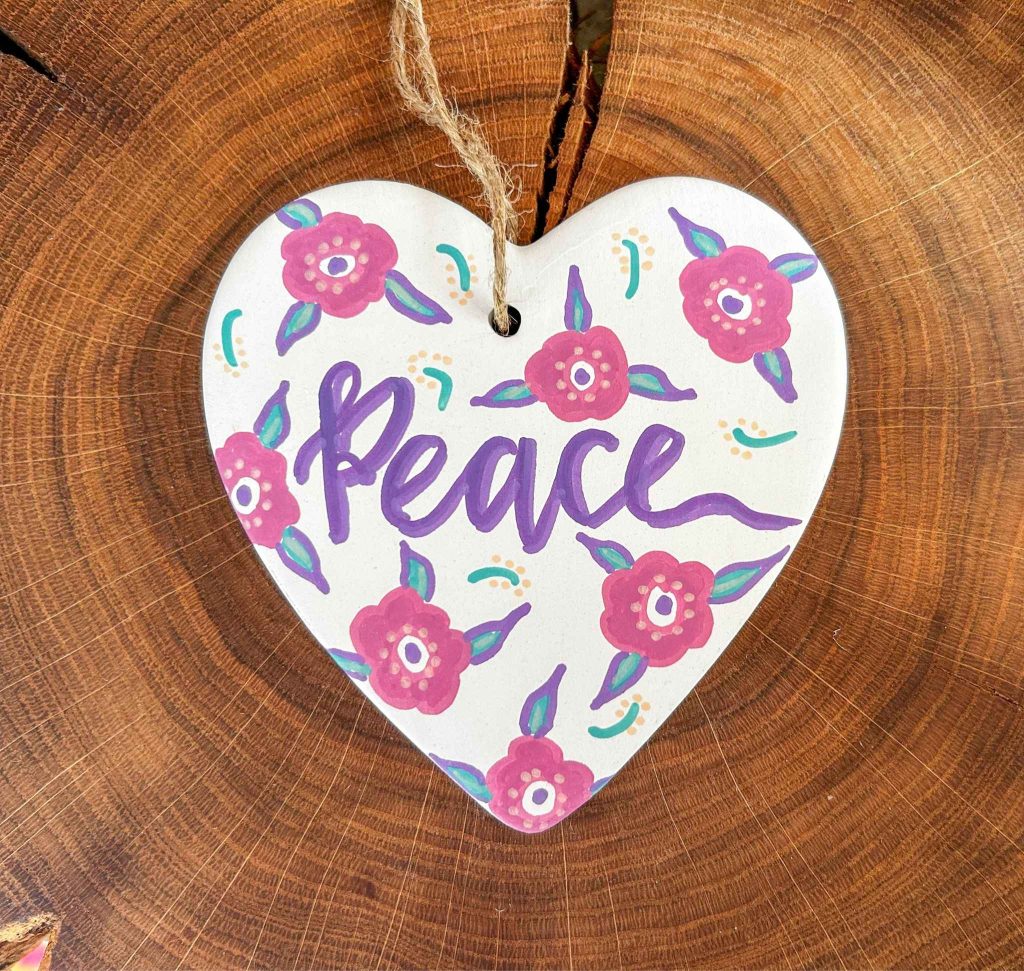 a white heart on a wooden background the heart has the word peace in purple and pink flowers around it